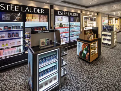 Ein Kosmetikgeschäft an Bord der Spectrum of the Seas. Beleuchtete Regale präsentieren Estée Lauder und Origins Produkte. Ein elegantes Ambiente mit gemustertem Teppich.