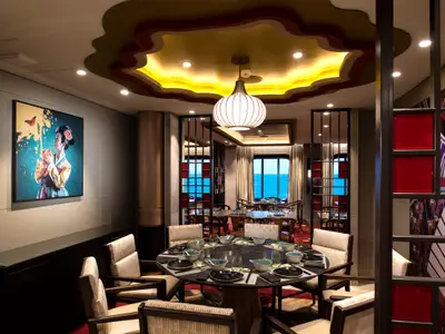 Elegantes asiatisches Restaurant an Bord der Spectrum of the Seas. Gedeckte Tische, großer Meerblick, eine markante Deckenbeleuchtung und ein Kunstgemälde prägen den Raum.