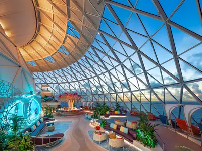 Blick in den AquaDome auf der Star of the Seas: Eine geräumige Lounge mit Bar, Sitzbereichen, Aquarien und einer großen Glaskuppel, die weiten Meerblick ermöglicht.