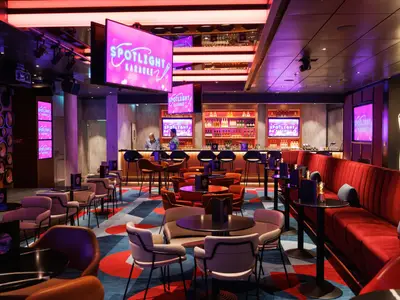 Ein Blick in die moderne Karaoke-Bar „Spotlight Karaoke“ an Bord der Star of the Seas mit Bar, zahlreichen Sitzbereichen, Monitoren und einem dekorativen Mikrofon an der Wand.