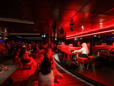 Ein stilvoller Innenbereich der Star of the Seas, beleuchtet in warmem Rot, zeigt zwei Pianistinnen an roten Flügeln auf einer Bühne. Eine Gruppe von Gästen sitzt vor der Bühne und verfolgt aufmerksam die musikalische Darbietung.
