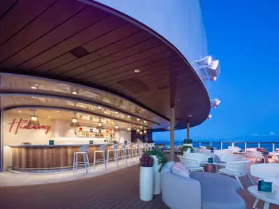 Auf der Star of the Seas: Beleuchtete Bar 'The Hideaway' und Lounge-Bereich auf dem Außendeck. Blick auf Meer und Dämmerungshimmel.