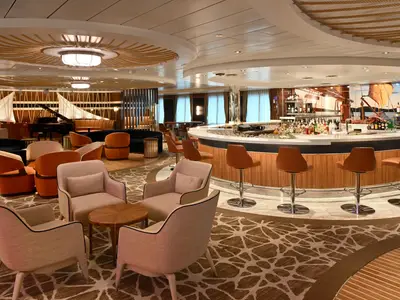 Bar- und Loungebereich auf der Star of the Seas. Eine große Bar, gemütliche Sessel und ein Klavier sind sichtbar. Maritime Elemente schmücken den modernen Innenraum.