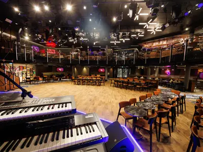 Blick in einen großen Live-Musik-Saal auf der Star of the Seas. Im Vordergrund stehen Keyboards auf einer Bühne. Der Saal verfügt über mehrere Ebenen mit Tischen, Stühlen und Lounge-Bereichen sowie Bars. Zahlreiche Scheinwerfer sind an der Decke montiert.