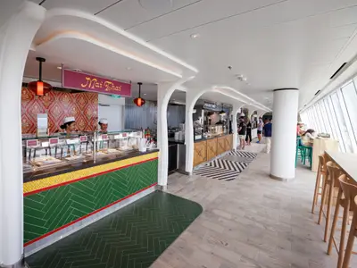 Buffetbereich auf der Star of the Seas mit Essensständen 'Mai Thai' und 'Pig Out BBQ', Personal und Gästen. Große Fenster bieten Meerblick, dazu moderne Sitzgelegenheiten.