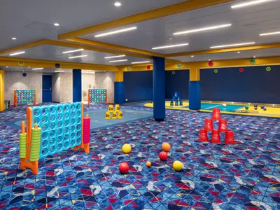 Der geräumige Kinder- und Familienspielbereich der Star of the Seas zeigt verschiedene Spiele wie Connect Four, Becherstapeln und Ballspiele auf blau gemustertem Teppichboden.