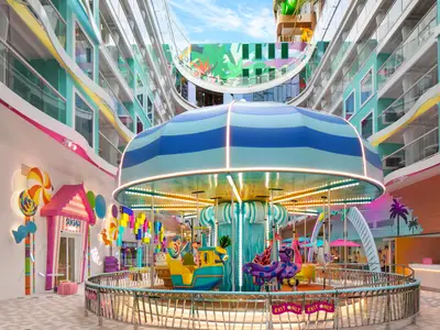 Zentrales Karussell und bunte Dekorationen auf einem Deck der Star of the Seas. Sichtbar sind ein Süßigkeitenladen, farbige Kabinenbalkone und tropische Wandmalereien.