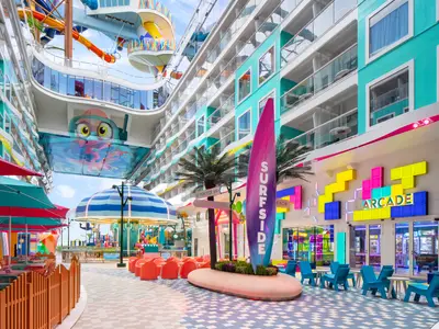Blick auf den farbenfrohen Surfside-Bereich der Star of the Seas mit einer Promenade, Spielhalle, Karussell und Essbereichen. Darüber hängt eine Oktopus-Kunstinstallation, flankiert von Balkonkabinen.