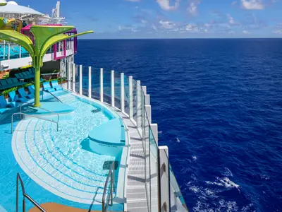 Poolbereich an Deck der Star of the Seas, umgeben von blauen Liegestühlen und grüner Struktur. Rechts, hinter Glas, das weite blaue Meer und ein bewölkter Himmel.