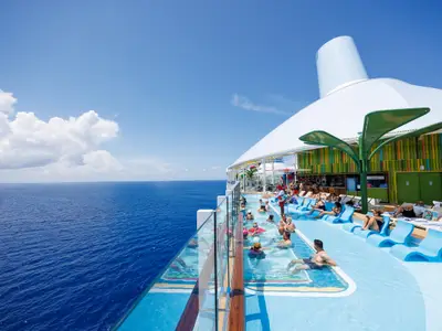 Auf dem Oberdeck der Star of the Seas entspannen sich Passagiere in einem Pool und auf blauen Liegen, mit weitem Blick auf den blauen Ozean und den Himmel.