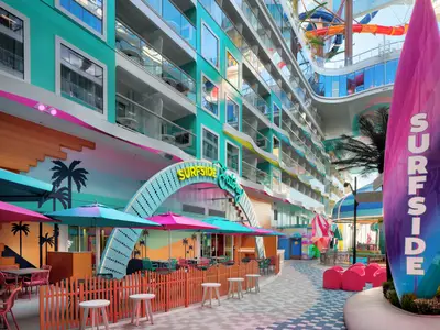 Surfside-Deckbereich der Star of the Seas mit Restaurants, bunten Sonnenschirmen und Palmenmotiven. Oben sind farbige Wasserrutschen sichtbar.