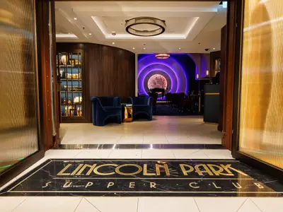 Blick durch offene Türen in den Lincoln Park Supper Club. Auf dem Marmorboden steht in Gold "Lincoln Park Supper Club". Innen befinden sich blaue Samtsessel, ein Bühnenbereich mit lila Licht und eine Bar.