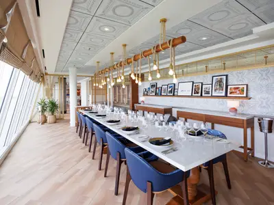 Innenansicht eines Restaurants an Bord der Star of the Seas. Ein langer Tisch mit blauen Stühlen, großen Fenstern und einer Holz-Seil-Lampe.