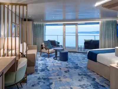 Blick in eine helle Kabine der Star of the Seas. Mit Balkon und Meerblick. Das Zimmer hat ein Bett, Sofa, Schreibtisch und blauen Teppich.
