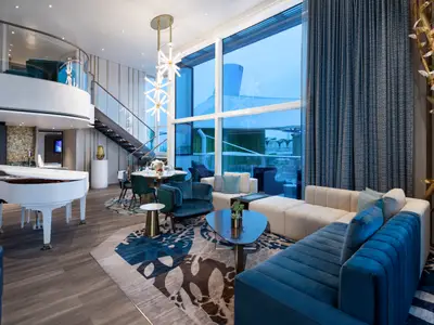 Innenansicht einer luxuriösen, zweistöckigen Suite der Star of the Seas. Zu sehen sind ein Flügel, ein Essbereich, ein Wohnzimmer mit blauen Sofas und großen Fenstern zum Meer.