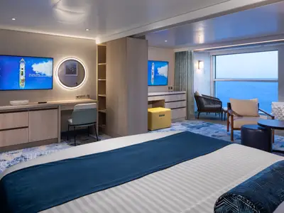 Suite auf der Star of the Seas: Schlafzimmer mit Bett, Schreibtisch mit TV, beleuchtetem Spiegel. Wohnbereich mit Sitzgelegenheiten und großem Fenster zum Meer.