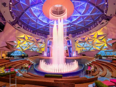 Der beleuchtete AquaDome der Star of the Seas zeigt einen zentralen Brunnen, umgeben von amphitheatraler Bestuhlung. Geometrische Decke, farbige Wände und Meerblick.