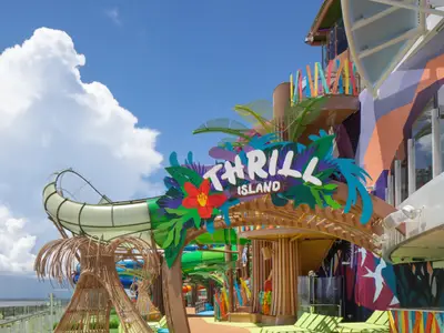 Der Freizeitbereich 'Thrill Island' auf der Star of the Seas: Buntes Eingangsschild, tropische Deko und eine Wasserrutsche unter blauem Himmel.