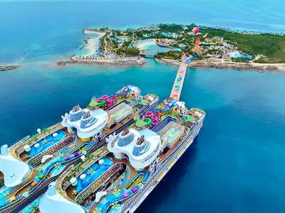 Luftaufnahme der Star of the Seas und eines Schwesterschiffs, vor einer tropischen Insel mit Wasserpark. Eine bunte Brücke verbindet die Schiffe direkt mit den Attraktionen des Resorts an Land.