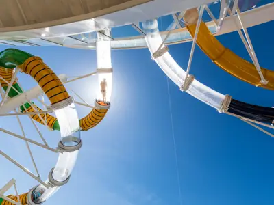 Nahaufnahme der mehrfarbigen Wasserrutschen auf der Symphony of the Seas unter blauem Himmel. Eine Person steht in einer transparenten Rutschenkapsel, bereit für den Start.
