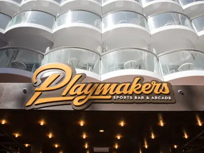 Das Schild der Playmakers Sports Bar & Arcade ist dominant. Dahinter die weißen, runden Balkone der Symphony of the Seas. Unten: dunkle Überdachung mit vielen kleinen Lichtern.