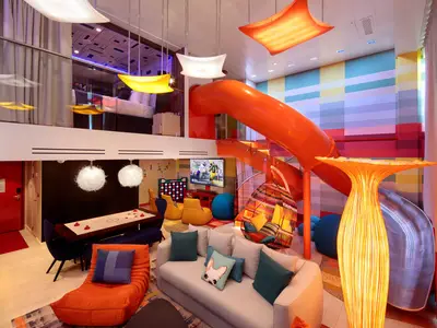 Eine lebendige, zweistöckige Suite an Bord der Symphony of the Seas. Zu sehen sind ein Schlafzimmer auf der oberen Ebene, eine orangefarbene Rutsche, die in den unteren Wohnbereich führt, mit Sofa, Spieltisch und Fernseher.