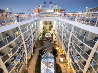 Abendlicher Blick auf den beleuchteten Central Park an Bord der Symphony of the Seas. Die begrünte Promenade ist von Balkonkabinen gesäumt.