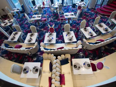 Vogelperspektive auf ein modern gestaltetes Restaurant mit bunten Schmetterlingsmustern auf dem Teppich. Es sind verschiedene Tische und Sofas mit bunten Kissen und Geschirr zu sehen.