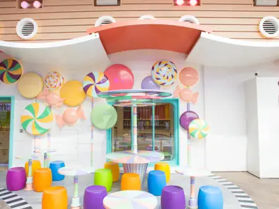 Innenbereich der Symphony of the Seas mit farbenfroher Süßigkeiten-Dekoration. Große Lutscher und Bonbons schmücken die Wände. Kleine Tische und bunte Hocker laden zum Verweilen ein.