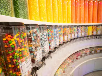 Süßigkeitengeschäft auf der Symphony of the Seas. Bunte Bonbons in hohen Röhren und transparenten Behältern auf geschwungenen Regalen.