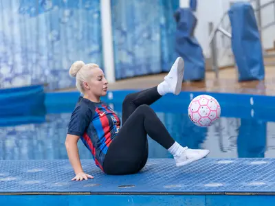 Eine Frau mit Trikot jongliert einen weiß-pinken Fußball auf einer blauen Plattform am Pool der Symphony of the Seas. Im Hintergrund sind blaues Wasser und eine Wand.