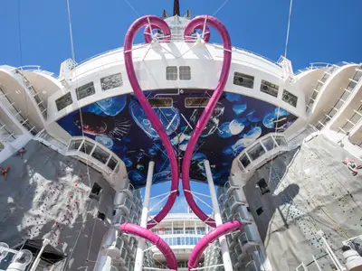Ansicht des Hecks der Symphony of the Seas mit zwei Kletterwänden, einer herzförmigen rosa Wasserrutsche und einem Unterwassermural mit Quallen. Mehrere Personen klettern.