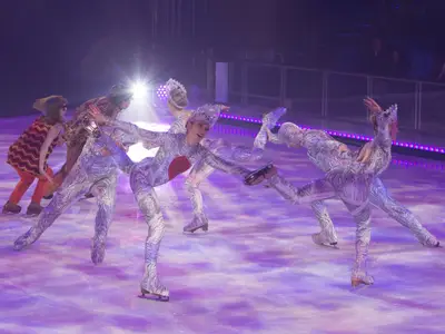 Mehrere Eiskunstläufer in aufwendigen, glitzernden Kostümen performen eine lebendige Eis-Show auf dem Eisring der Symphony of the Seas. Die Szene ist dramatisch beleuchtet mit lila Farbtönen.
