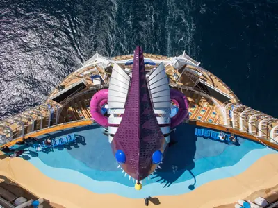 Luftaufnahme des Bugs der Symphony of the Seas, die einen Anglerfisch-förmigen Rutschenkomplex und zwei rosa Wasserrutschen auf dem Deck zeigt, umgeben vom blauen Meer.