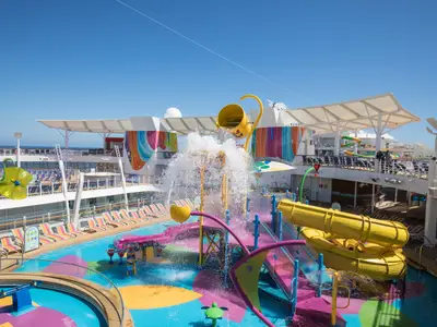 Das Kinder-Wasserparadies auf dem Deck der Symphony of the Seas. Bunte Rutschen, ein Kippeimer und Pools unter blauem Himmel.
