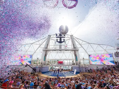 Feier an Bord der Utopia of the Seas: Konfettiregen fällt auf ein Publikum im AquaTheater, Personen auf der Bühne, Royal Caribbean Logo sichtbar.