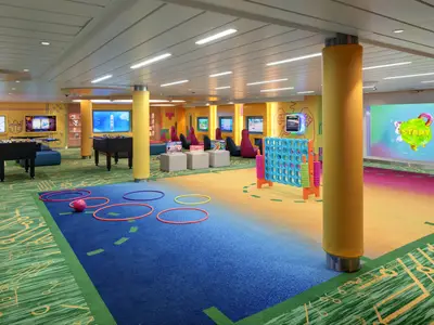 Heller, farbenfroher Spielbereich auf der Utopia of the Seas mit Foosballtischen, Bildschirmen, Connect Four und Hula Hoops auf mehrfarbigem Teppichboden.