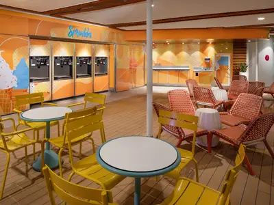 Der farbenfrohe Sprinkles-Eisdielenbereich der Utopia of the Seas mit mehreren Selbstbedienungs-Eismaschinen. Gelbe Tische und Stühle sowie rote Korbsessel auf Holzboden prägen das Bild.