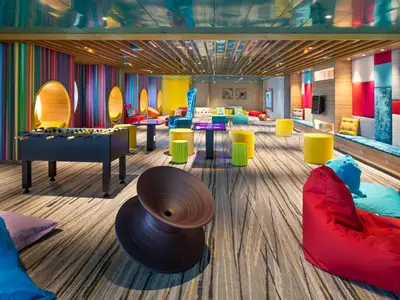 Moderner, farbenfroher Lounge-Bereich auf der Utopia of the Seas mit Kickertisch, bunten Sitzsäcken, Hockern und interaktiven Tischen, umgeben von lebhaften Wandgestaltungen.