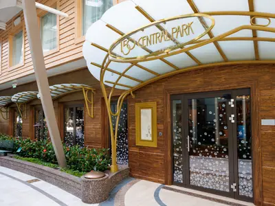 Der elegante Eingang des Restaurants 150 Central Park. Goldene Schriftzüge über einer gläsernen Überdachung, dunkle Holzwände und große Fenster mit Blumenmustern prägen das Bild.