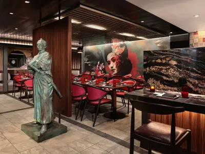 Das asiatische Restaurant auf der Utopia of the Seas, mit einer Samurai-Statue, roten Stühlen, einem Wandgemälde und einer Bar.