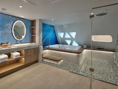 Geräumiges Badezimmer auf der Utopia of the Seas mit Whirlpool, großer begehbarer Dusche und Doppelwaschbecken. Moderne Einrichtung mit blauen Details und stimmungsvoller Beleuchtung.