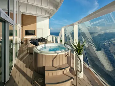 Geräumiger Außenbereich auf der Utopia of the Seas. Es gibt einen Whirlpool, Lounge-Sitzplätze, eine Bar und einen Wand-TV. Eine Glasbrüstung bietet weiten Meerblick.