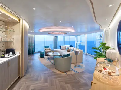 Blick in eine luxuriöse Suite der Utopia of the Seas. Der Wohnbereich bietet Meerblick, Sofa, Sessel, Minibar und Anrichte.