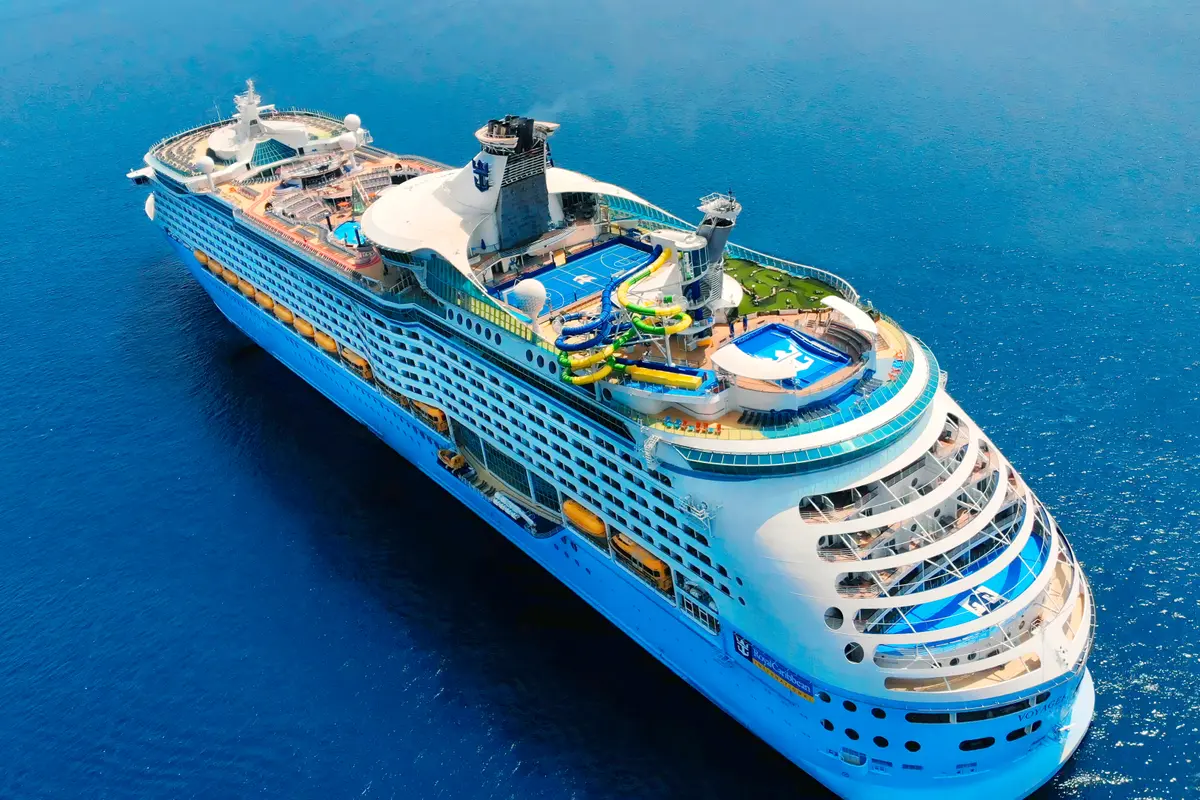 Luftaufnahme der Voyager of the Seas von Royal Caribbean im blauen Meer. Oben: Wasserrutschen, Pools, Sportfeld. Seitlich: Kabinen, Rettungsboote.