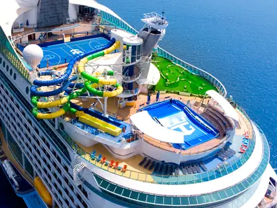 Luftaufnahme des Heckdecks der Voyager of the Seas mit Wasserrutschen, Sportplatz, Minigolf und Surfsimulator auf dem blauen Meer.