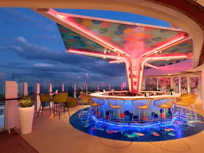 Abendliche Ansicht einer beleuchteten Outdoor-Bar auf der Wonder of the Seas. Die Bar hat eine bunte Decke, blaue Lichter an der Theke und Blick aufs Meer.