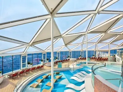 Blick in das überdachte Solarium der Wonder of the Seas mit mehreren Pools, Sonnenliegen und großflächigen Fenstern zum Meer bei Tageslicht.