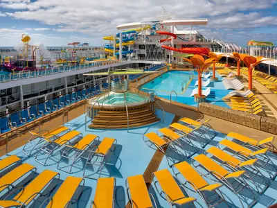 Das belebte Oberdeck der Wonder of the Seas mit Pool, Whirlpool, orangefarbenen Liegen, farbigen Wasserrutschen und einem Wasserspielplatz unter blauem Himmel.