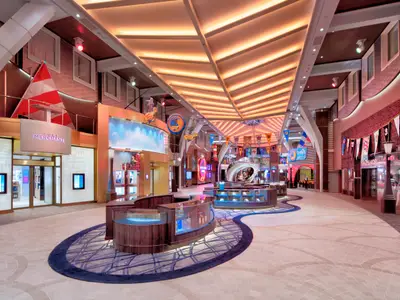 Die Royal Promenade der Wonder of the Seas. Geschäfte, Vitrinen und maritime Dekorationen. Ein blaues Teppichmuster führt durch den hellen, modernen Gang.
